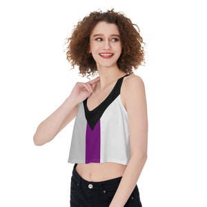 May include: A white crop top with a black and purple design. The top has a V-neck and thin straps.