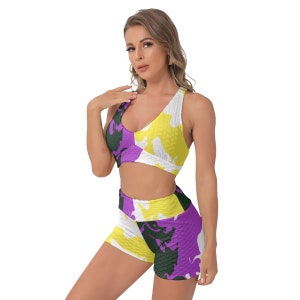 Könnte beinhalten: Ein zweiteiliges Workout-Set mit Sport-BH und Shorts. Das Set hat ein lebendiges Camouflage-Muster in Gelb, Lila, Weiß und Dunkelgrün. Der Sport-BH hat einen V-Ausschnitt, und die Shorts sind hoch tailliert.