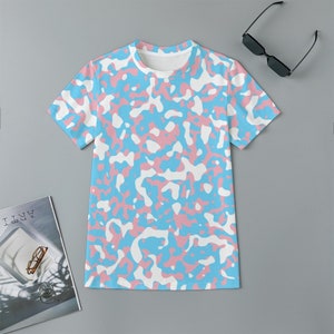Könnte beinhalten: Ein kurzärmeliges T-Shirt mit einem Camouflage-Muster in Hellblau, Rosa und Weiß. Das Shirt hat einen Rundhalsausschnitt und ist aus einem weichen, wahrscheinlich atmungsaktiven Stoff gefertigt. Sonnenbrille auf der rechten Seite des Shirts.
