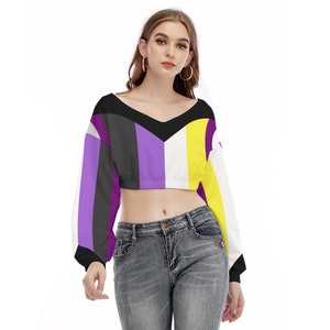 May include: A cropped long-sleeve shirt with a v-neck and a striped pattern in purple, black, white, and yellow. The shirt is a cropped style, ending above the waist.