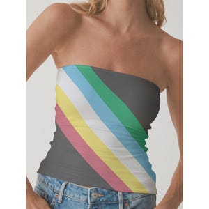 Könnte beinhalten: Ein trägerloses Tube-Top mit diagonalem Streifenmuster. Das Oberteil hat Streifen in verschiedenen Farben, darunter Grau, Grün, Blau, Weiß, Gelb, Rosa und Schwarz. Das Oberteil wird mit einer blauen Jeans getragen.