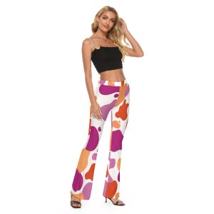 May include: A black crop top with a silver chain strap and white, flared pants. The pants feature a colorful pattern of large, abstract shapes in shades of orange, pink, and purple. The model is wearing black sandals.