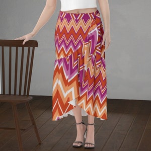 May include: A wrap skirt featuring a vibrant chevron pattern in shades of red, orange, pink, and white. The skirt has a ruffled hem and a wrap design. The model is wearing black high-heeled sandals.