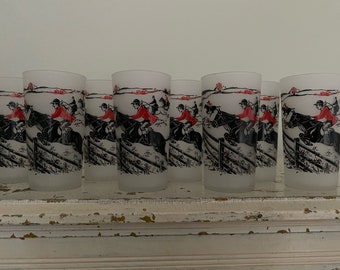 May include: Set of eight frosted glass tumblers with a black and white illustration of riders on horses jumping over a fence. The riders are wearing red jackets and white pants.