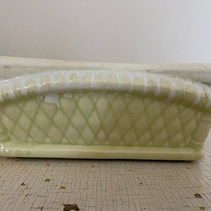 May include: A pale green ceramic planter with a diamond-shaped lattice pattern and a white glaze. The planter has a rectangular shape with rounded edges.