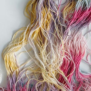 Puede incluir: Primer plano de hilo de bordar colorido en tonos amarillos, rosas, morados y blancos. Los hilos est&aacute;n dispuestos en un haz suelto y enredado, creando una exhibici&oacute;n texturizada y vibrante. Ideal para proyectos de manualidades y bordado.