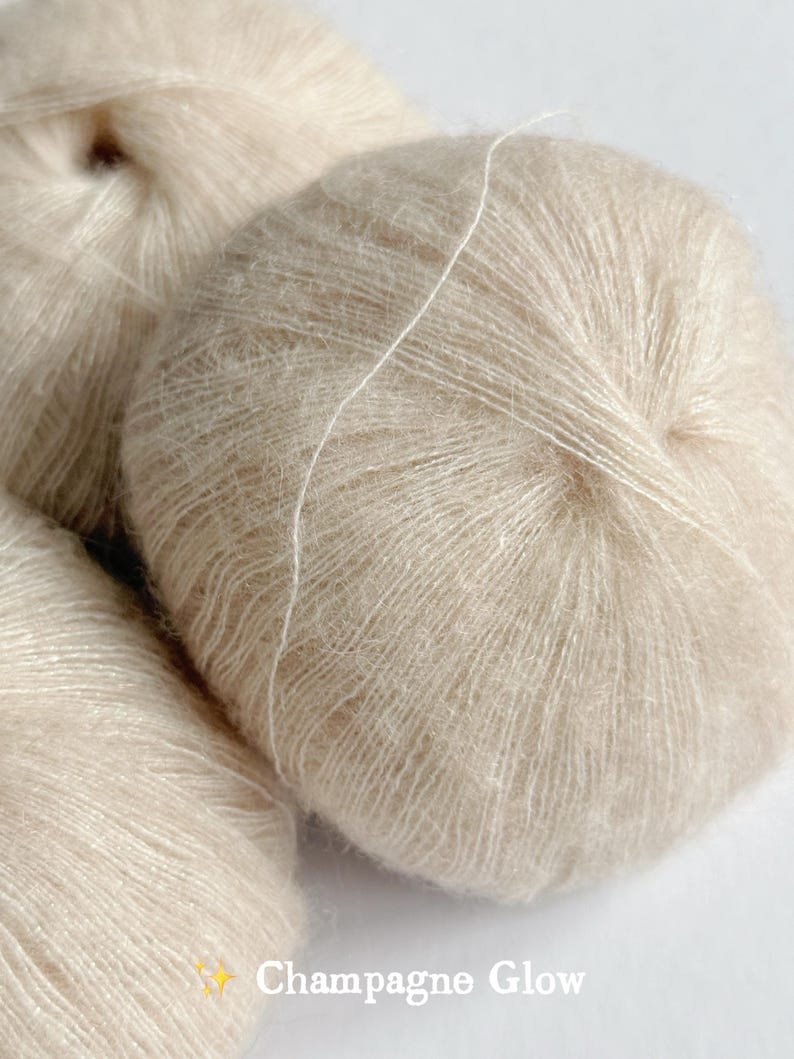 Puede incluir: Primer plano de varias madejas de hilo beige. El hilo tiene una textura suave y esponjosa y un ligero brillo. El texto "Champagne Glow" es visible en la esquina inferior derecha.