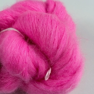 May include: A close-up of a vibrant pink yarn ball. The yarn has a soft, fuzzy texture and a bright, saturated color. A white thread is wrapped around the yarn. Ideal for knitting and crochet projects.