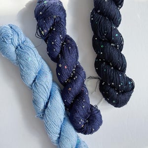 Peut inclure: Trois écheveaux de fil bleu. Le fil est torsadé et texturé, avec un écheveau bleu clair et deux écheveaux bleu foncé. Les écheveaux foncés sont ornés de paillettes argentées, ajoutant une touche de brillance.