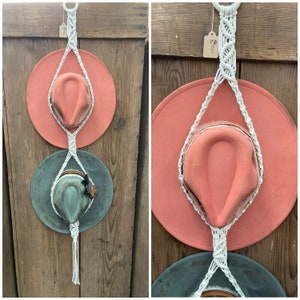 May include: Two hats hanging on a white macrame hat rack. The top hat is a light pink color and the bottom hat is a light green color. The macrame hat rack is hanging on a wooden wall.