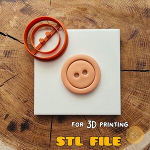 May include: An orange circular cookie cutter with a crossbar and two small cylindrical posts, alongside a light peach-colored circular button shape with two holes. The text FOR 3D PRINTING STL FILE is visible at the bottom of the image.