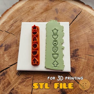 May include: An orange plastic multi-shape cutter tool featuring a star, heart, lock, at symbol, shield, and arrow, alongside a light green clay strip embossed with the same six shapes. The text FOR 3D PRINTING STL FILE is visible.