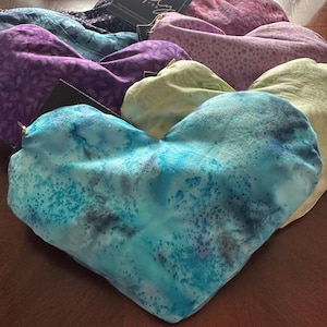May include: A collection of heart-shaped pillows in various colors and patterns, including blue, purple, green, and white. The pillows are made of fabric with a tie-dye effect.