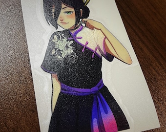 Può includere: Una donna con lunghi capelli neri indossa un vestito nero e viola con ricami floreali bianchi. Il vestito ha un colletto alto e una cintura viola. La donna guarda la telecamera e ha un leggero sorriso sul viso.