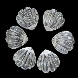 Könnte beinhalten: Sechs klare, muschelförmige Glasperlen, kreisförmig vor schwarzem Hintergrund angeordnet. Jede Perle hat ein geripptes, fächerartiges Design, das ein strukturiertes Aussehen erzeugt. Die Perlen sind durchscheinend.
