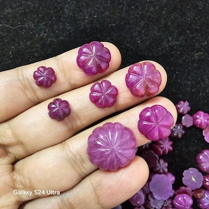 May include: A collection of pink flower-shaped gemstones, some are larger than others, and are arranged on a hand. The gemstones are smooth and polished.