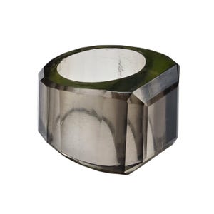 Op de afbeelding: Een brede, robuuste ring gemaakt van doorschijnend, rookgrijs materiaal. De band heeft een gefacetteerde, geometrische buitenkant met scherpe, hoekige randen en een gladde, cirkelvormige opening aan de binnenkant voor een gedurfde, solide uitstraling.