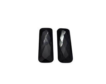 May include: Two black, rectangular-shaped gemstones with faceted surfaces. The gemstones have a polished, reflective appearance, and are set against a white background. The gemstones are likely for jewelry making.