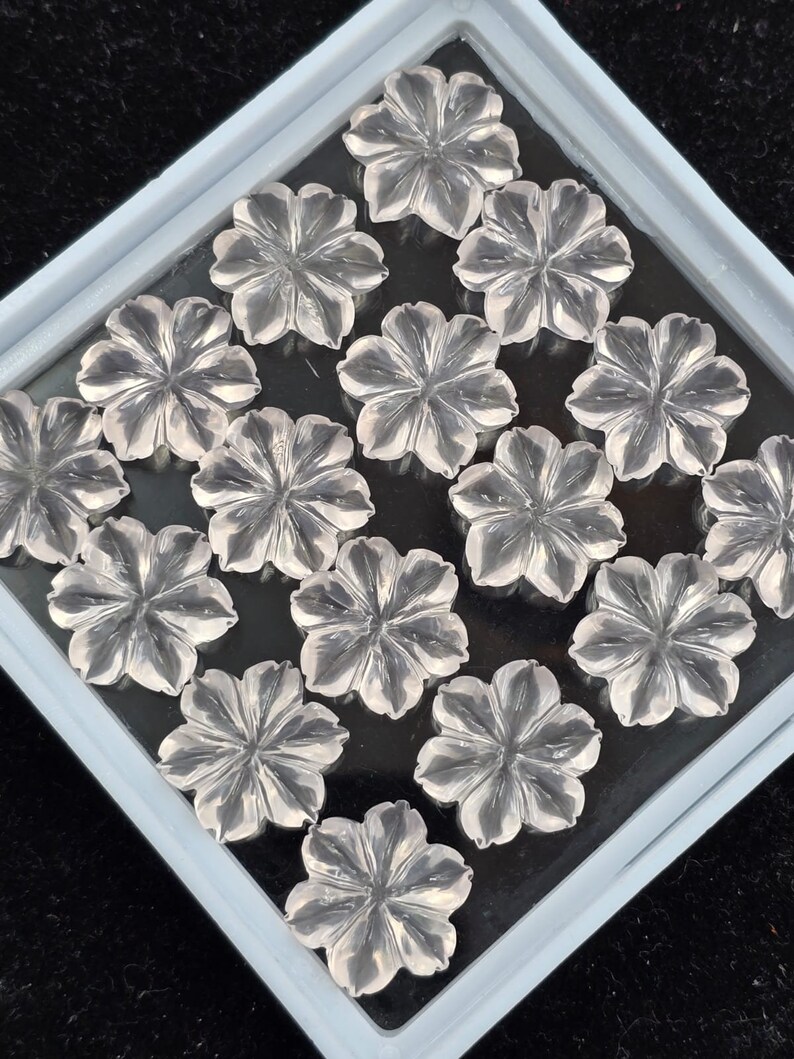 K&ouml;nnte beinhalten: Eine Sammlung von klaren Quarz-Blumencabochons in einer wei&szlig;en Schale. Die Cabochons sind in einem Gittermuster angeordnet.