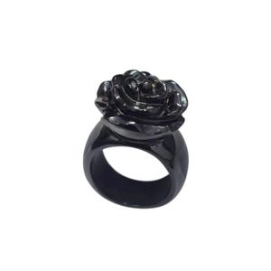 Könnte beinhalten: Ein schwarzer Ring mit einem Rosen-Design. Der Ring hat ein dickes Band und eine detaillierte florale Oberseite, was ein kühnes und elegantes Schmuckstück ergibt. Der Ring besteht aus einem dunklen, möglicherweise metallischen Material.
