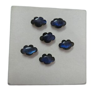 Könnte beinhalten: Sechs regenbogenfarbene blaue und schwarze cabochons in Wolkenform auf einer weißen Oberfläche.
