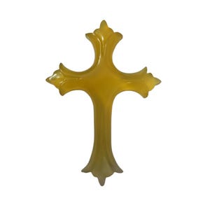 May include: A decorative cross in a light yellow hue. The cross has ornate, pointed edges on each arm and at the base. The design is symmetrical and stands out against the white background.