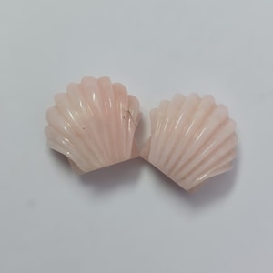 Op de afbeelding: Twee roze schelpvormige kristallen sculpturen. De schelpen zijn glad en hebben een delicaat, gedetailleerd ontwerp.