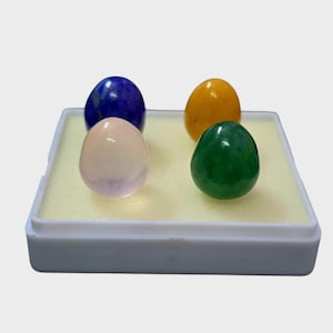 Puede incluir: Cuatro huevos de piedras preciosas pulidas en una vitrina blanca. Los huevos son en tonos de azul, amarillo, rosa y verde. La vitrina tiene un interior amarillo claro.