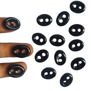May include: A collection of black oval buttons with two holes each. The buttons are scattered on a white background.