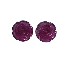 May include: Two dark purple rose-shaped objects. Each rose is carved with detailed petals and a spiral center. The objects are set against a plain white background, highlighting their intricate design and color.