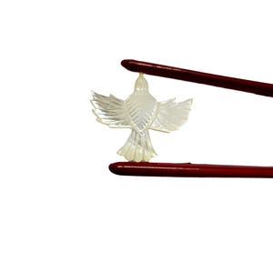 May include: A translucent, carved bird pendant with outstretched wings is held by two red chopsticks against a white background. The bird has detailed feather patterns and a small loop at the top for hanging. The chopsticks are dark red.