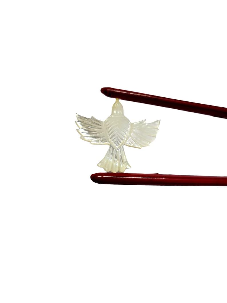 May include: A translucent, carved bird pendant with outstretched wings is held by two red chopsticks against a white background. The bird has detailed feather patterns and a small loop at the top for hanging. The chopsticks are dark red.