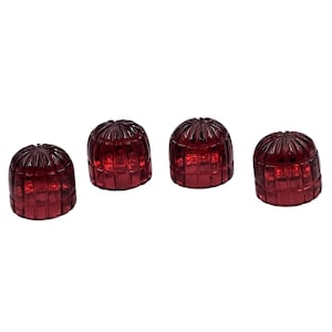 May include: Four red glass candle holders. Each holder has a domed shape with a grid-like pattern. The glass appears to be transparent, allowing light to pass through. The candle holders are arranged in a row against a white background.