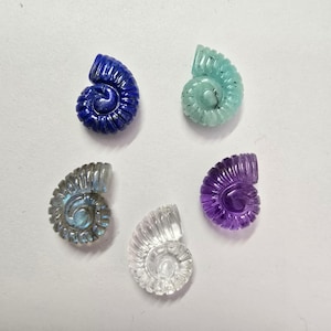 May include: Six carved gemstone ammonite shell pendants in various colours, including blue, green, grey, clear, and purple.