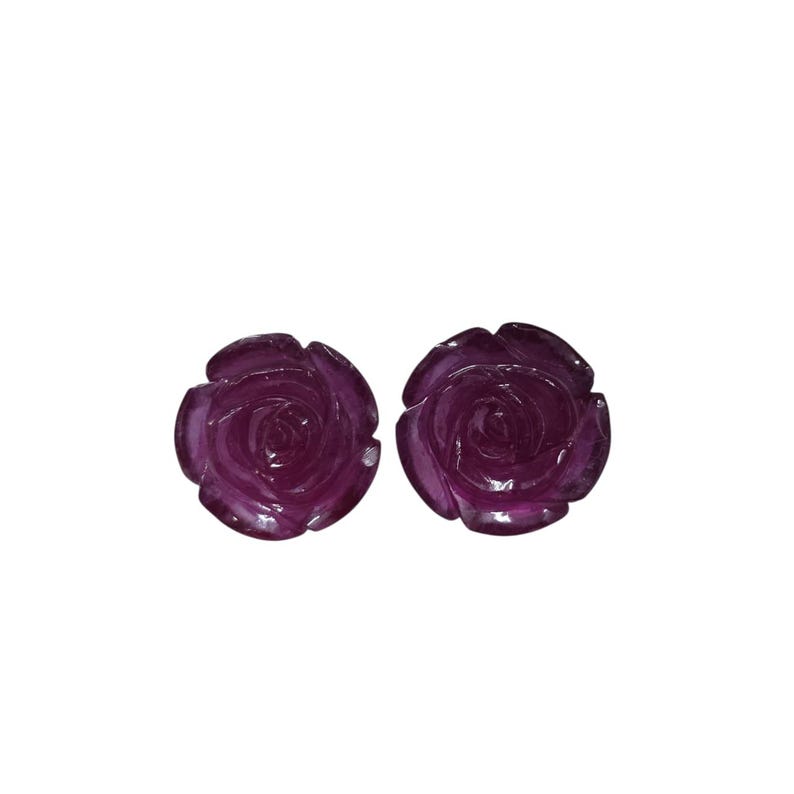 May include: Two dark purple rose-shaped objects. The objects have detailed petal carvings and a glossy finish. The roses are set against a white background. The objects appear to be decorative or jewelry components.