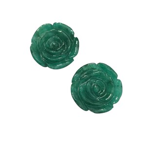 May include: Two carved emerald green rose-shaped gemstones. The gemstones are detailed with petals and a spiral center. The roses are set against a white background. These gemstones could be used for jewelry or decorative purposes.