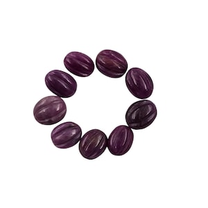 May include: A collection of ten oval-shaped, carved gemstones arranged in a circle. The stones are a deep purple color with lighter purple and brown streaks. Each stone has a series of parallel grooves carved into its surface.