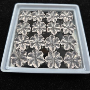 K&ouml;nnte beinhalten: Eine Schale mit 15 klaren, facettierten, rosafarbenen Quarz-Blumencabochons. Die Cabochons sind in einem Gittermuster angeordnet.