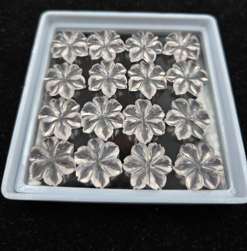 K&ouml;nnte beinhalten: Eine Schale mit 15 klaren, facettierten, rosafarbenen Quarz-Blumencabochons. Die Cabochons sind in einem Gittermuster angeordnet.