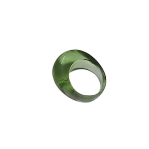 Op de afbeelding: Een transparante, olijfgroene ring met een afgeronde, ovaalvormige bovenkant. De ring is gemaakt van een glad, glanzend materiaal en heeft een dikke band. De ring staat tegen een effen witte achtergrond.