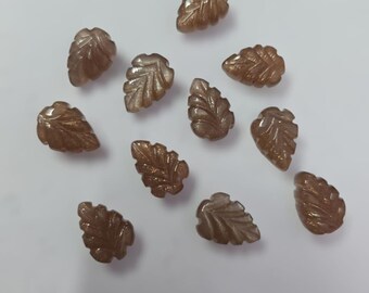 May include: A collection of twelve brown sunstone leaf-shaped cabochons. The stones are translucent and have a shimmery, iridescent quality.