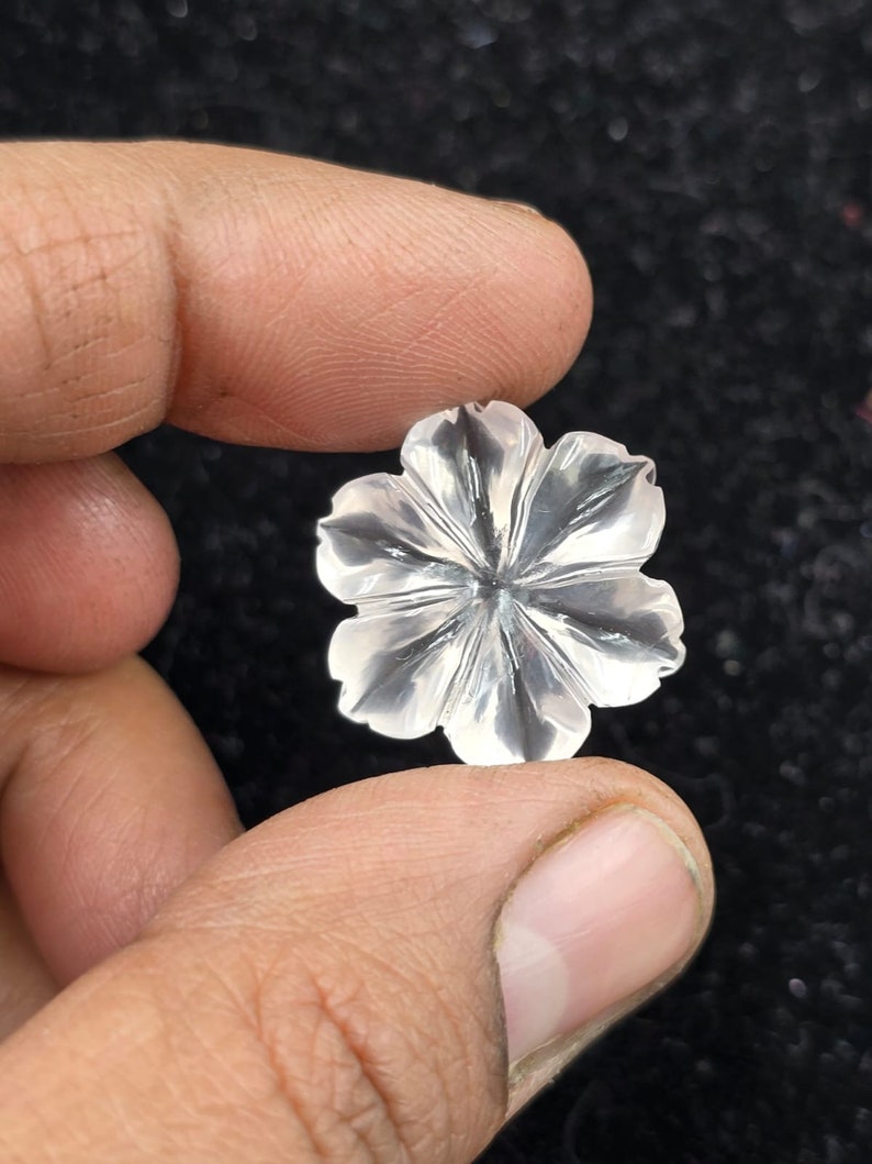 K&ouml;nnte beinhalten: Ein klarer Quarzkristall, der in Form einer Blume geschnitzt ist. Die Blume hat f&uuml;nf Bl&uuml;tenbl&auml;tter und eine Mitte mit einem Sternmuster.