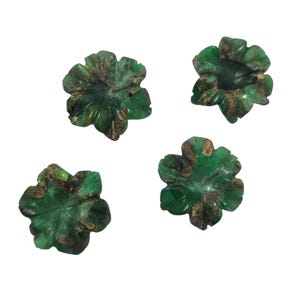 May include: Four carved green gemstone flower-shaped objects with brown accents. Each flower has detailed leaf-like patterns and a polished finish. The objects are arranged against a white background.