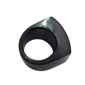 May include: A black ring with a geometric design. The ring has a smooth, polished surface and a triangular shape on top. The ring is made of a solid, dark material.