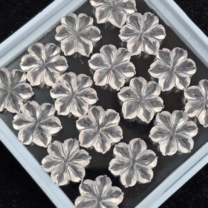 K&ouml;nnte beinhalten: Eine Sammlung von klaren Quarz-Blumencabochons in einer wei&szlig;en Schale. Die Cabochons sind in einem Gittermuster angeordnet.