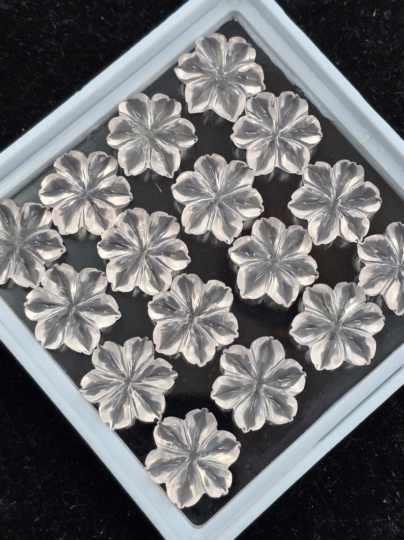K&ouml;nnte beinhalten: Eine Sammlung von klaren Quarz-Blumencabochons in einer wei&szlig;en Schale. Die Cabochons sind in einem Gittermuster angeordnet.