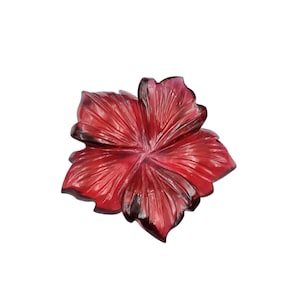 May include: A translucent, deep red glass flower ornament featuring five distinct petals with intricate, radiating carved lines. The material has a glossy finish with varying shades of crimson and dark burgundy, creating a dimensional effect.
