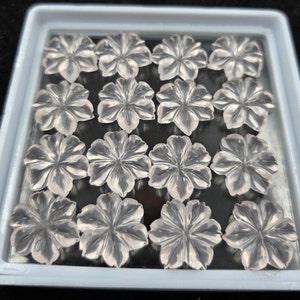 K&ouml;nnte beinhalten: Eine Sammlung von 15 klaren Quarz-Blumencabochons in einer wei&szlig;en Plastik-Schale. Die Cabochons sind durchscheinend und haben einen leicht rosafarbenen Farbton.