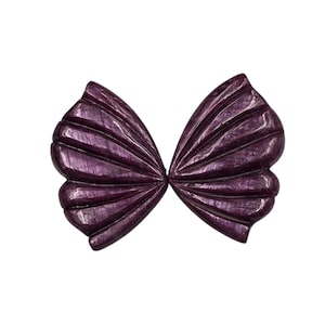 May include: A decorative, purple bow-shaped object with a textured, ridged surface. The bow has a symmetrical design, with each side mirroring the other. The object is set against a plain white background.