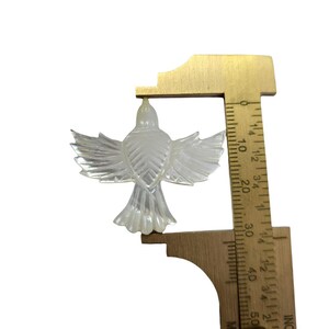 May include: A clear, iridescent bird-shaped ornament with outstretched wings. The ornament is being measured with a ruler, showing a height of approximately 2 inches. The bird has detailed feather patterns and a textured surface.